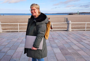 Marketing-Freelancerin und Autorin des Beitrags steht-mit-PC unter dem Arm in Travemünde am Pier.